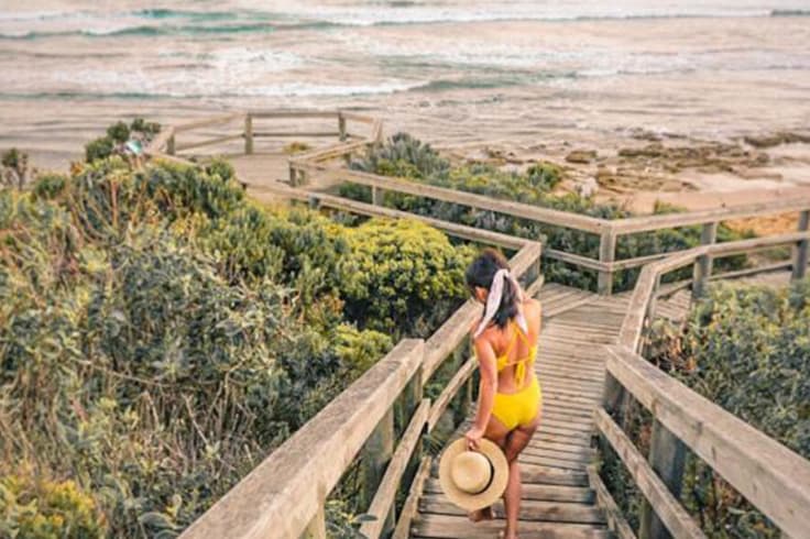 7 day road trip itinerary adelaide to melbourne 3 girl in swimsuit walks down steps at beach in australia