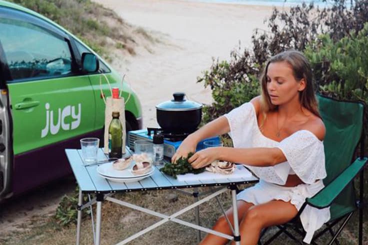 best time of year to visit australia 1 woman eating dinner next to a jucy campervan travelling in summer