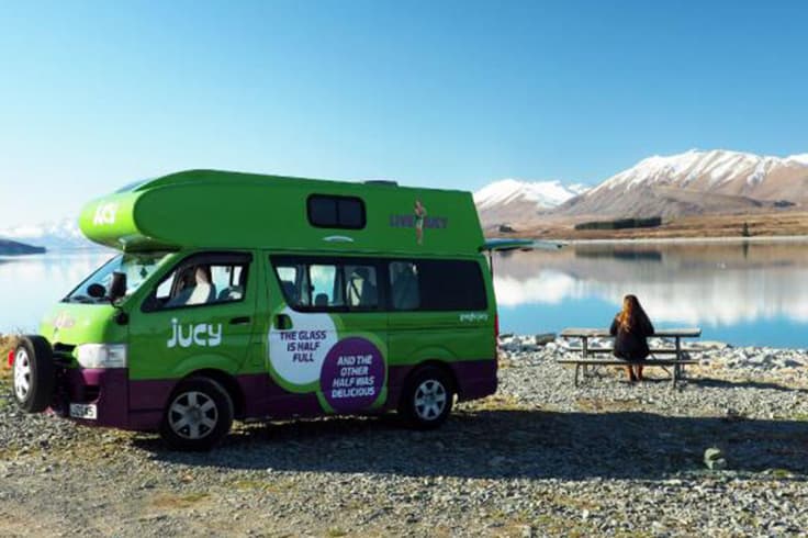 what to expect when travelling nz in winter 2 Woman sitting at a camping table next to campervan mountains and lake